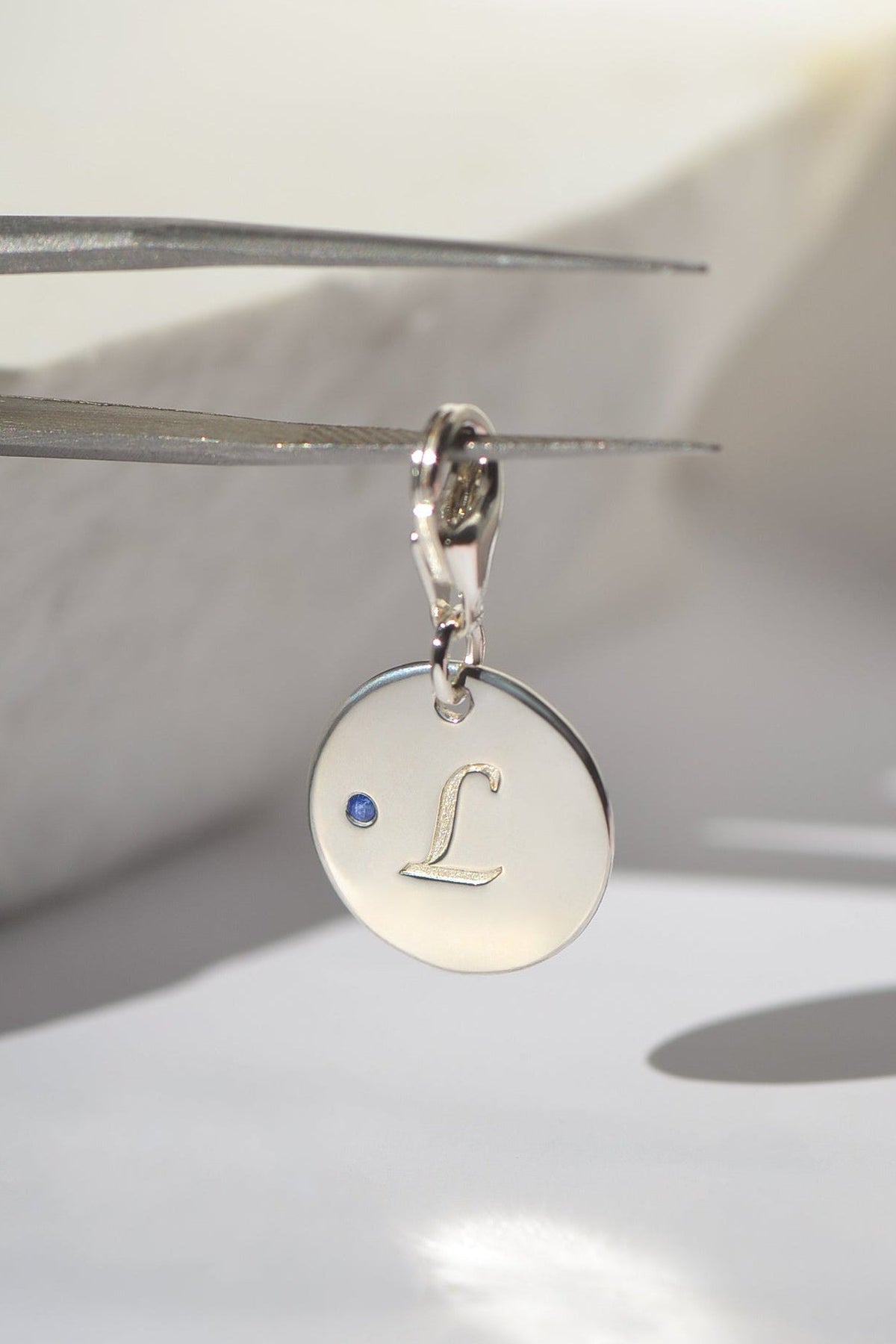 REINE by PAWVÉ. A solid sterling silver pendant, with a natural round brilliant cut blue sapphire, engraved with the pet's initial 'L'. Fine jewellery for pets.